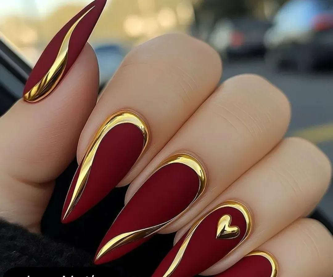 This design is all about bold sophistication. A matte crimson base on sharp, stiletto nail extensions is accented with raised, metallic gold lines and a single gold heart. It's a powerful and luxurious look, perfect for a glamorous reception or cocktail event.