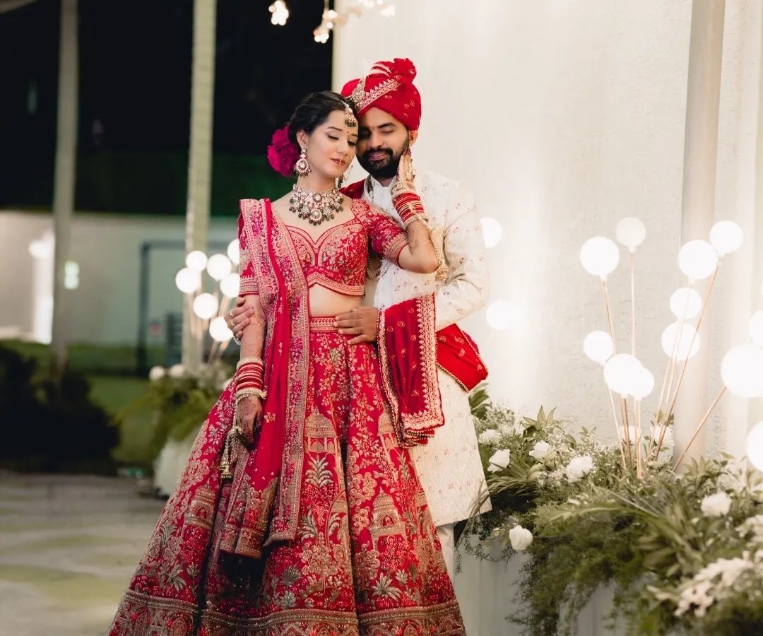 A fairytale moment brought to life. The bride's magnificent red lehenga and the groom's elegant sherwani create a stunning portrait against a backdrop of warm, festive lights, showcasing our expertise in capturing grand North Indian weddings.