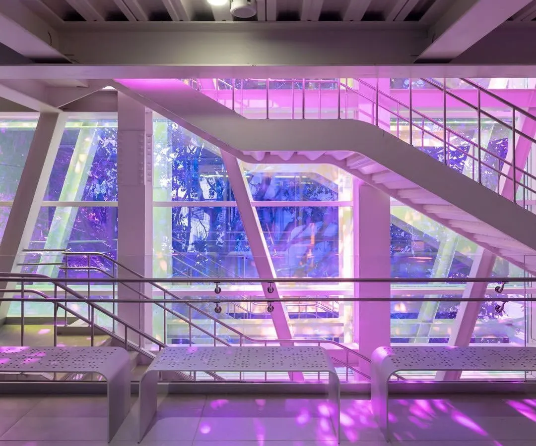 The central staircase at the Museum of Art and Photography (MAP) in Bengaluru, where dichroic film on the glass facade bathes the space in shifting colors. This element turns a simple circulation area into a dynamic experience of light, reflecting our belief that even functional parts of a building can be joyful and inspiring.