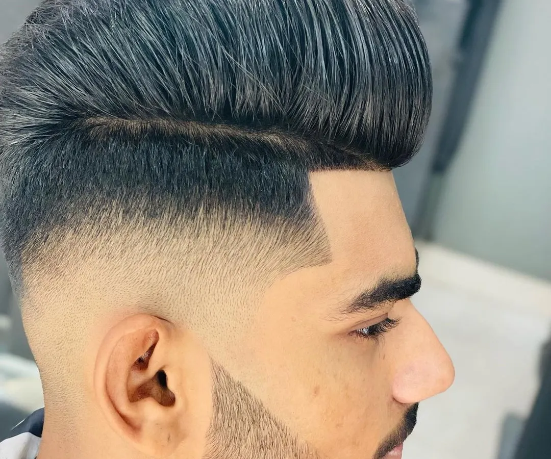 A perfect example of a high-volume pompadour with a skin fade that blends seamlessly into the beard. Every line is clean, sharp, and intentional, creating a powerful, modern look.