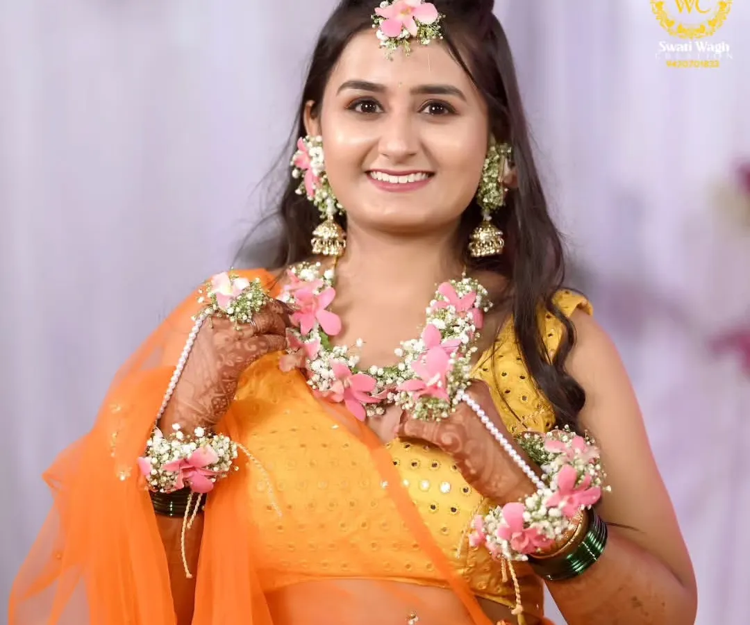 A radiant Haldi bride glowing in our custom-designed floral jewellery. This set, featuring delicate pink flowers and baby's breath, is handcrafted to perfectly complement the vibrant orange of her outfit, making her Haldi ceremony truly unforgettable.