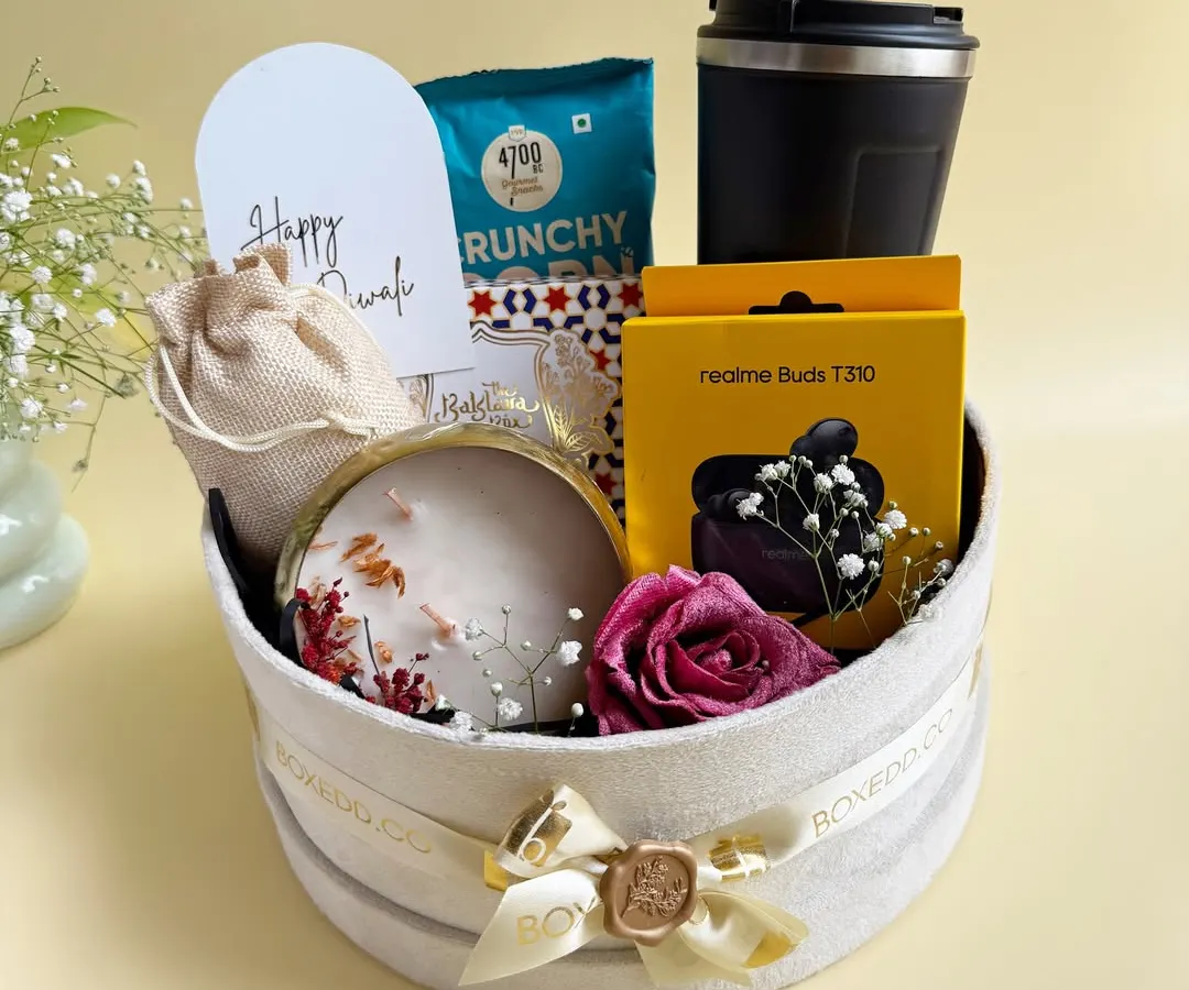 I love mixing modern utility with festive tradition. This hamper features high-quality electronics like Realme Buds alongside artisanal sweets, a scented candle, and gourmet snacks, all presented in a beautiful velvet box.
