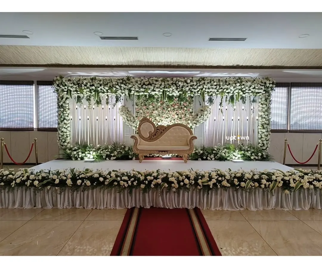 We design elegant stages for engagements and receptions that feel both grand and personal. This setup features a full floral frame of white rose's and lush green's, a classic diwan for the couple, and professional stage lighting to create a beautiful focal point for the event.