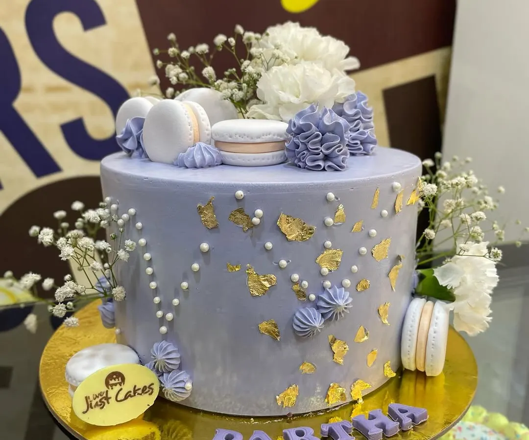 This elegant lavender cake is a beautiful example of a sophisticated design for a special occasion. It features delicate gold leaf accents, piped buttercream details, and is tastefully adorned with fresh baby's breath flowers and perfectly crafted macarons.