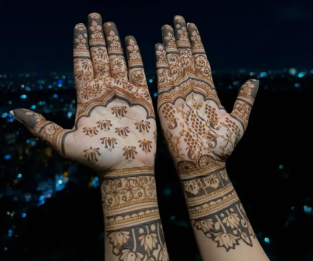 The palm-side view of Divya Spandana's mehendi, showing a mix of traditional butis and intricate floral work. One hand features a detailed peacock, while the other has scattered florals for a unique, asymmetrical style.