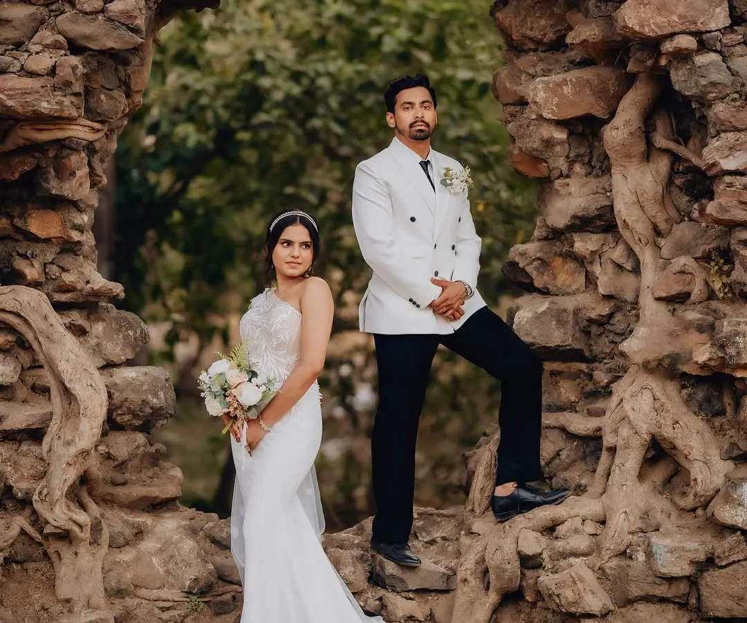 Karen and Abhijeet framed by a natural stone archway in Goa. This shot combines formal wedding attire with a rustic, historic location for a powerful, editorial-style portrait.