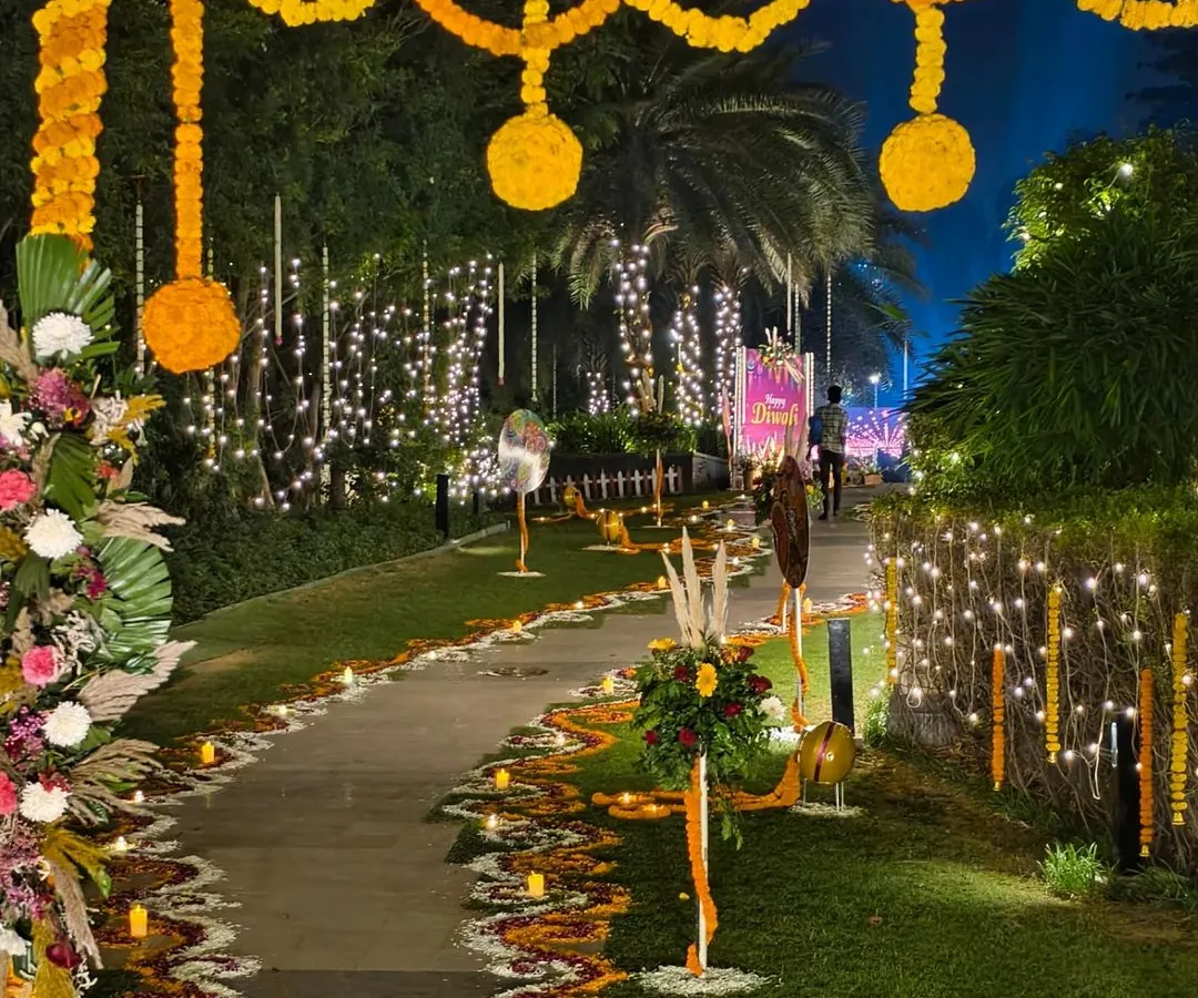 A stunning entrance and walkway for a large-scale outdoor Diwali party. We used extensive flower rangoli, hanging marigold garlands, and warm fairy lights to create a grand and welcoming path for guests.