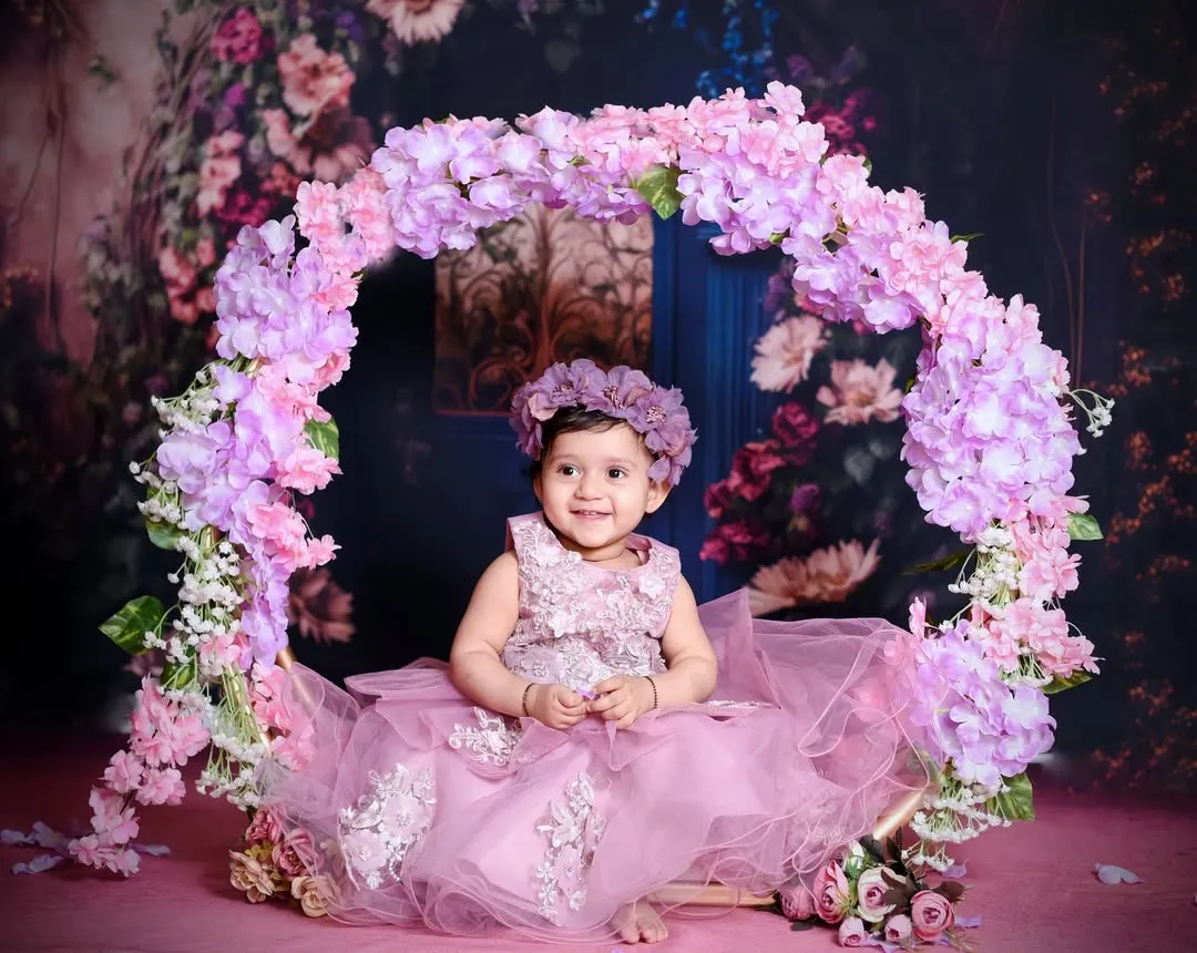 For this pre-birthday shoot, we created a dreamy floral wonderland. This little one is sitting on a beautiful swing adorned with pink and purple flowers, creating a magical portrait.