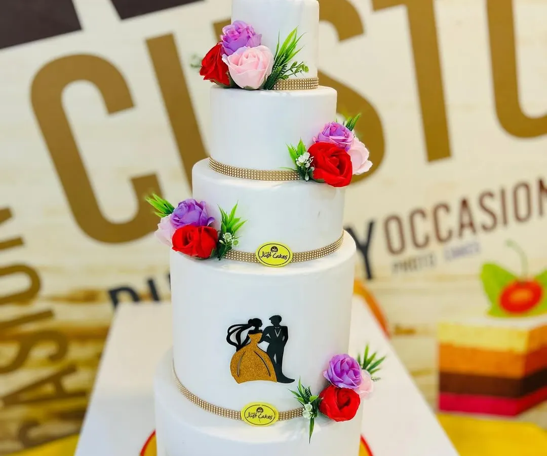 This grand 10kg, five-tiered wedding cake is a perfect example of classic elegance. Each tier is finished with smooth white fondant and decorated with delicate, colorful sugar flowers and a silhouette of a couple, showcasing our ability to create large, stunning cakes for your most important day.