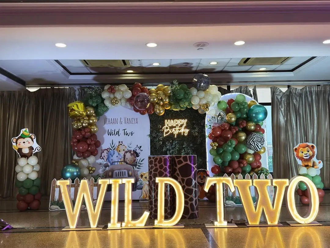 When the theme is "Wild Two," we go all out. This jungle safari setup for twins Vihaan and Vaniya features a lush green foliage backdrop, a custom balloon arch with animal print accents, and bold, illuminated "WILD TWO" marquee letters that set the stage for a roaring good time.