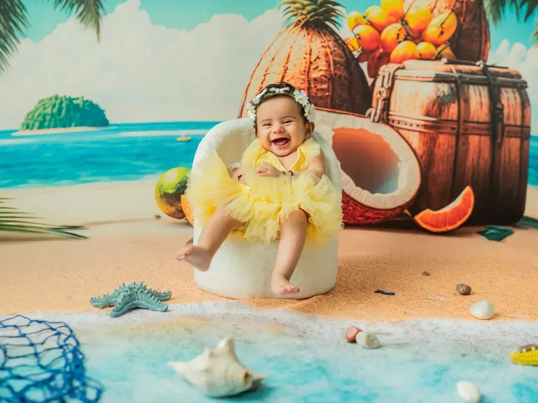 Nothing beats a genuine, happy laugh. This 'Beach Baby' setup is a favorite for sitter sessions, using a vibrant backdrop, soft sand, and themed props to create a fun, summery vibe in my Thane studio any time of year.