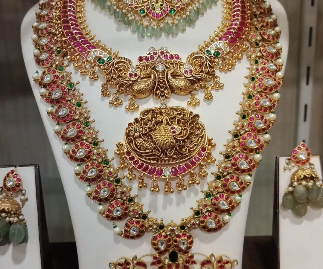 This is a complete South Indian bridal set, featuring traditional temple jewellery designs with intricate peacock motifs. The set includes a choker, a long haram, a stunning pendant, matching jhumkas, and a maang tikka, all crafted to look like authentic gold.
