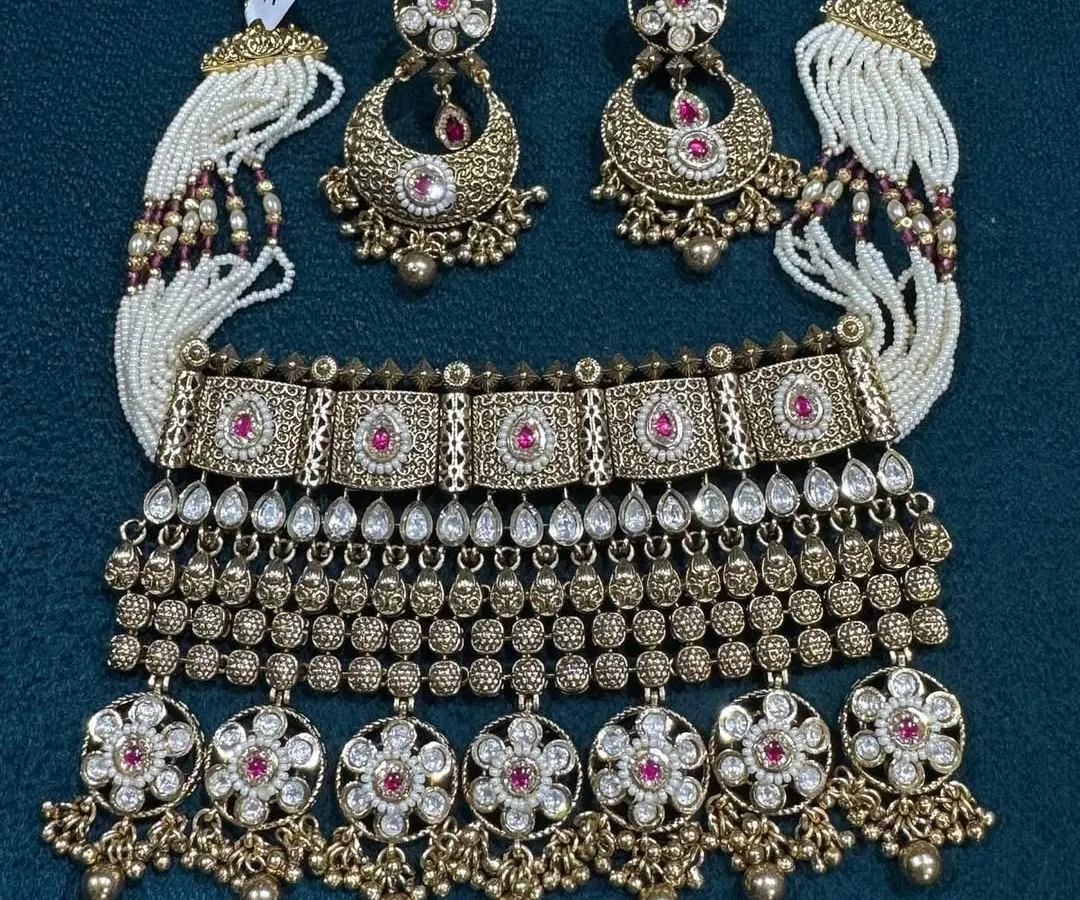 I love the craftsmanship on this antique finish choker set. The design has very detailed work with ruby-colored stones and is paired with beautiful chandbali earrings and delicate pearl strings, giving it a complete and traditional look.
