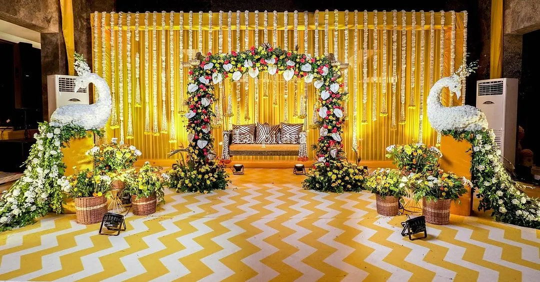 For this vibrant Teej celebration, we created a stunning stage featuring a backdrop of traditional marigold garlands. The setup was flanked by magnificent peacocks sculpted from white flowers, set against a chevron-patterned floor, blending classic Indian motifs with a modern aesthetic.