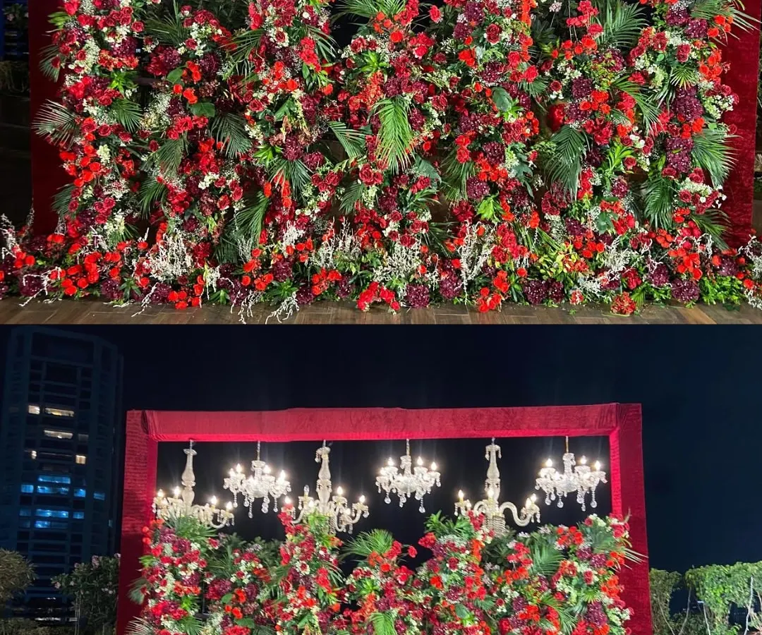 A truly dramatic reception stage featuring a dense wall of red florals and lush greenery, crowned with elegant crystal chandeliers. This design creates an atmosphere of pure opulence and romance for a grand celebration.