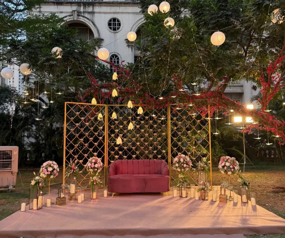 For this outdoor reception, I created a romantic seating area under the stars. The setup features a plush pink sofa against a golden lattice backdrop, surrounded by glowing candles and hanging paper lanterns that cast a warm, magical light. This design shows how I can transform an open lawn into an intimate and enchanting space for your special moments.