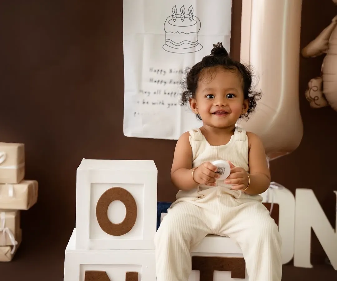 A classic first birthday portrait. This little one's bright smile shines in a charming, neutral-toned setup featuring "ONE" blocks and a sweet teddy bear theme.