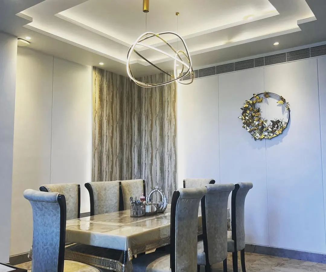 For this dining area, the goal was to create a space that feels both grand and intimate. The multi-layered tray ceiling with concealed lighting adds architectural depth, while the modern sculptural chandelier serves as a stunning centerpiece. The combination of a marble-top table, plush upholstered chairs, and subtle wall textures results in a luxurious setting for family meals.