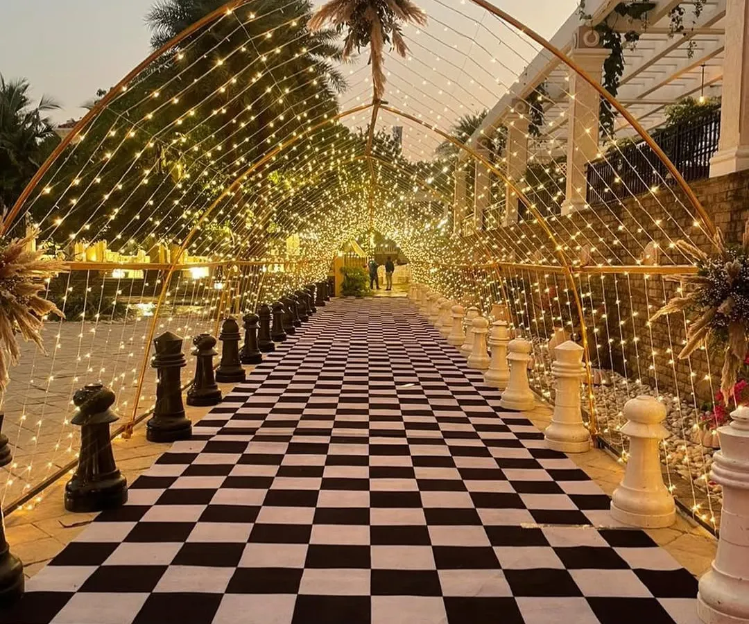 Making a magical first impression with this unique chess-themed entrance. The checkered walkway, lined with giant chess pieces and illuminated by a tunnel of fairy lights, created an unforgettable welcome for guests at this sangeet night.