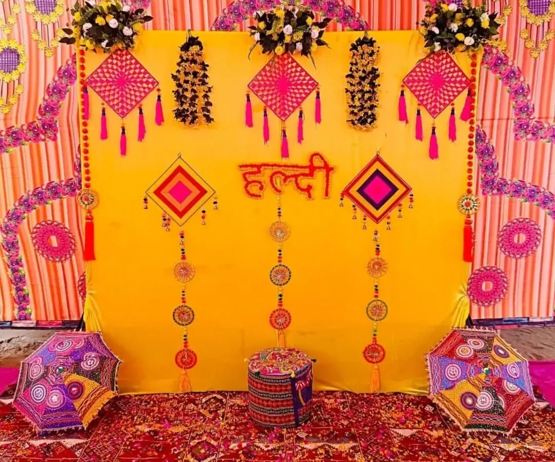 This is a classic Haldi ceremony backdrop I created, filled with traditional elements. The vibrant yellow cloth is decorated with colorful tassels and Rajasthani-style umbrellas, creating a festive and picture-perfect setting for your home function.