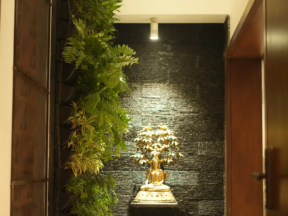We create tranquil corners by blending nature with art. This vertical garden is paired with a spotlit Buddha statue against a dark, textured wall, creating a focal point of peace and serenity in a modern hallway.