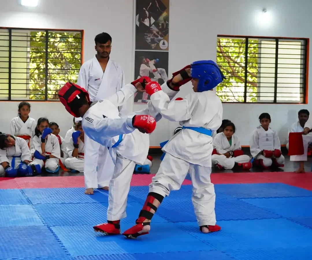 Two of our young students engage in a controlled sparring match during a belt exam, complete with protective gear. We teach competitive karate with a strong emphasis on safety and sportsmanship.