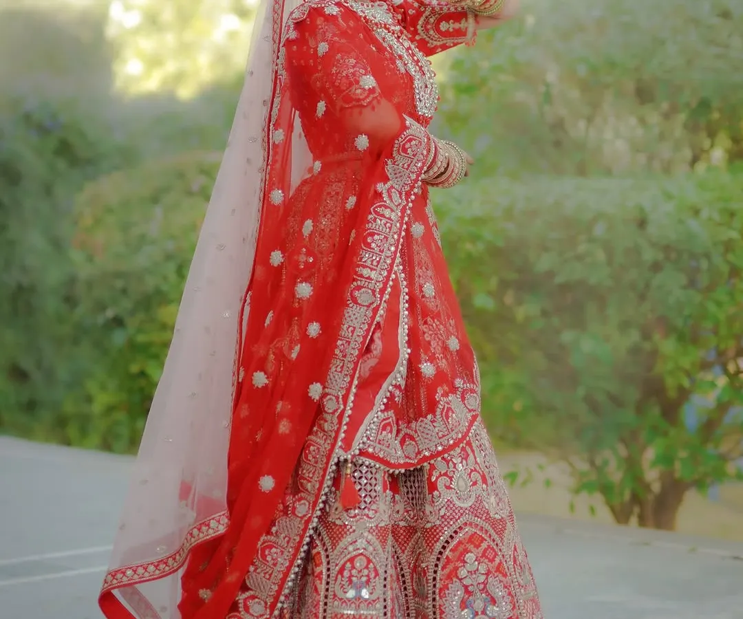 A full-length, fine-art bridal portrait showcasing the intricate details of a traditional red lehenga. I focus on classic poses and natural light to create elegant and timeless images of the bride on her special day.