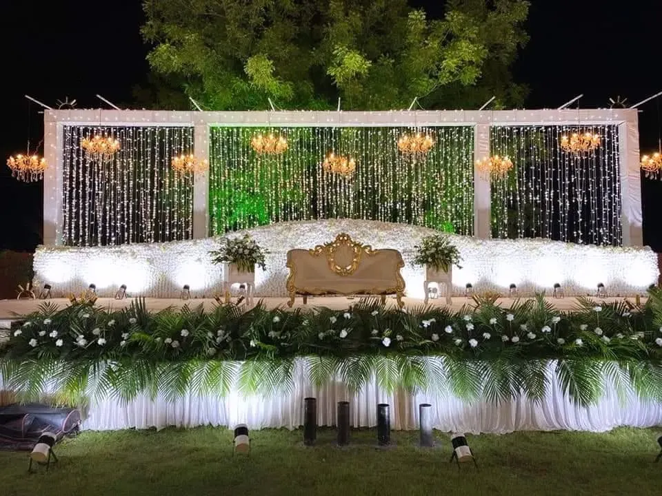 For this outdoor reception, I designed an elegant stage featuring cascading crystal strings, grand chandeliers, and a lush base of white flowers and greenery, creating a magical ambiance under the open sky.