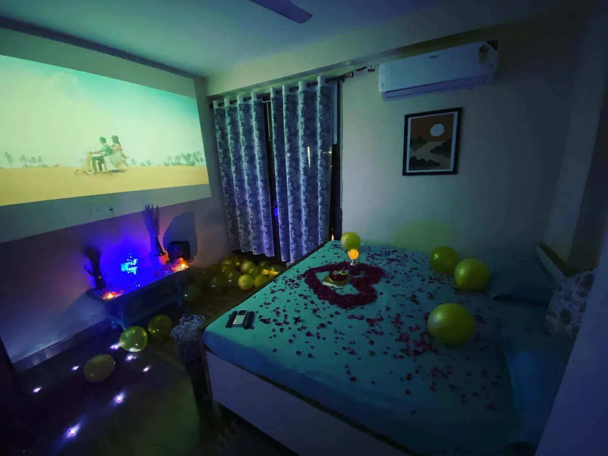 Here is the ultimate private movie night setup. The bedroom transforms into your personal cinema with a huge projector screen, while the bed is decorated with rose petals and surrounded by balloons, all under cozy, atmospheric lighting.