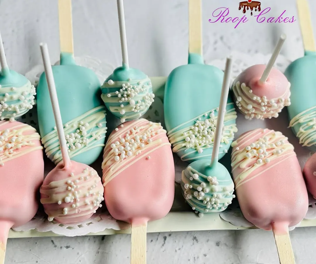 These modern cakesicles and cake pops are perfect for a gender reveal party. The treats are coated in pink and blue chocolate, finished with a white chocolate drizzle and pearl sprinkles for a touch of elegance.