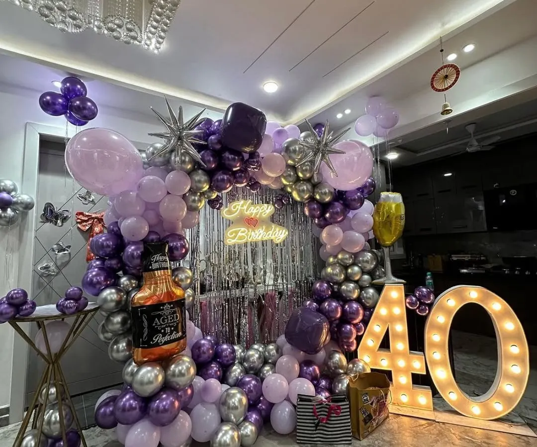 For this 40th birthday, we went for a classy and fun theme. The setup includes a balloon arch in purple and silver, a shimmer curtain backdrop, large marquee numbers, and even a fun whiskey bottle foil balloon to match the party vibe.