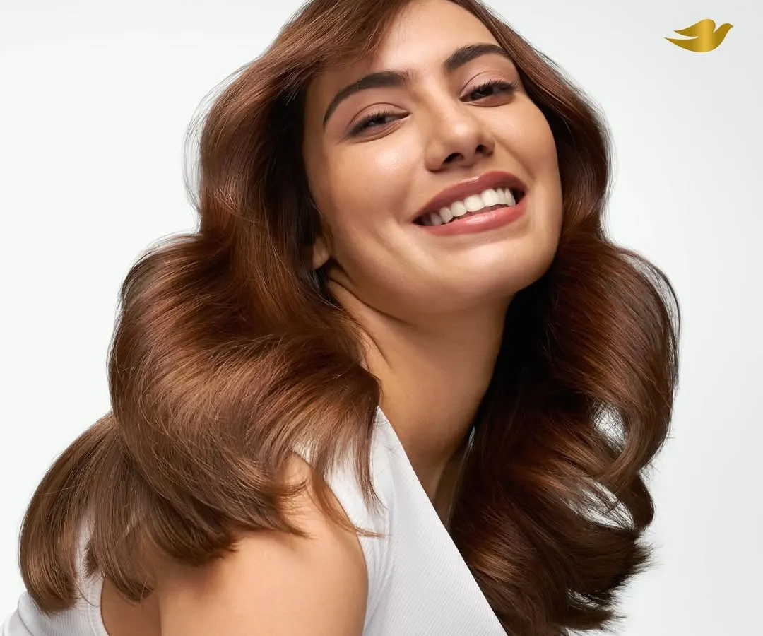 A clean, luminous studio photograph for a Dove haircare campaign. This image captures a model with healthy, voluminous brown hair and a joyful expression, highlighting the product's ability to create shine and vitality. The bright, high-key lighting is characteristic of my advertising work for major FMCG brands.