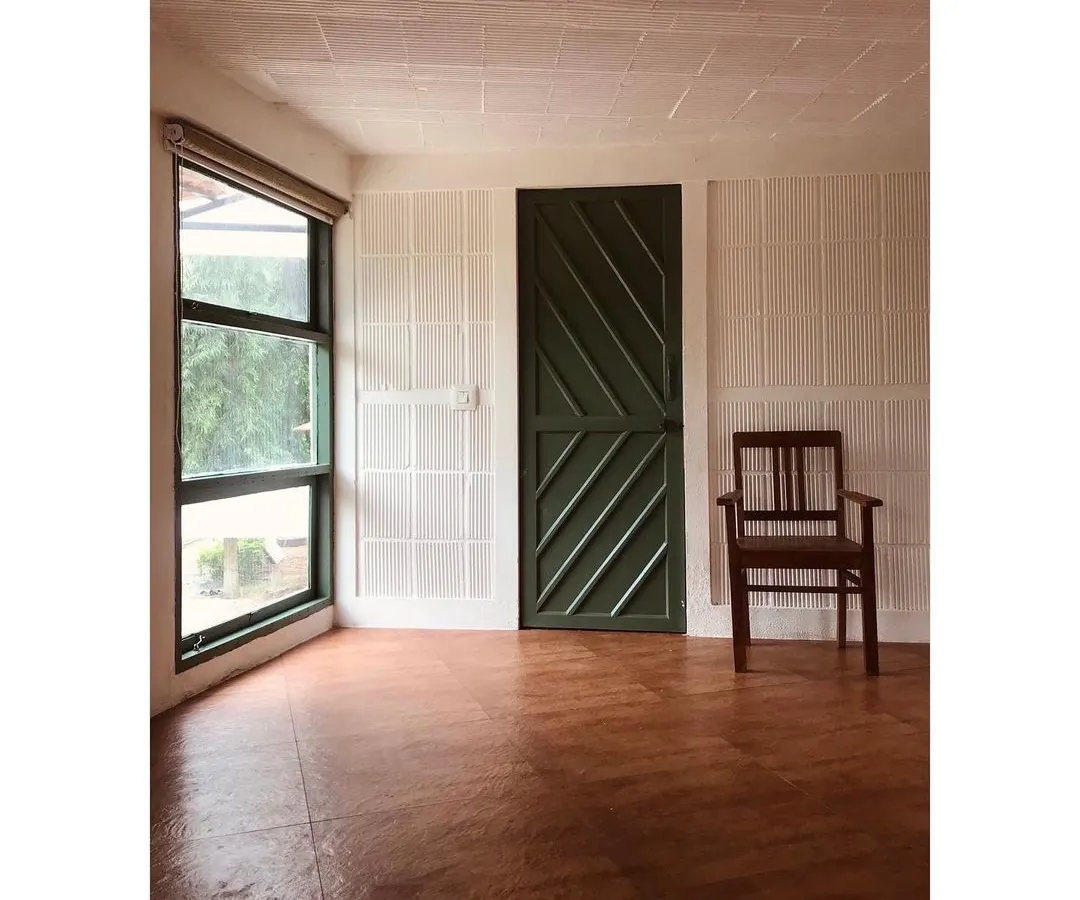 An interior view of a private farmhouse project, showcasing a minimalist aesthetic. The space is defined by its clean lines, an earthy oxide floor, and a large window that fills the room with natural light, creating a serene connection with the outdoors.