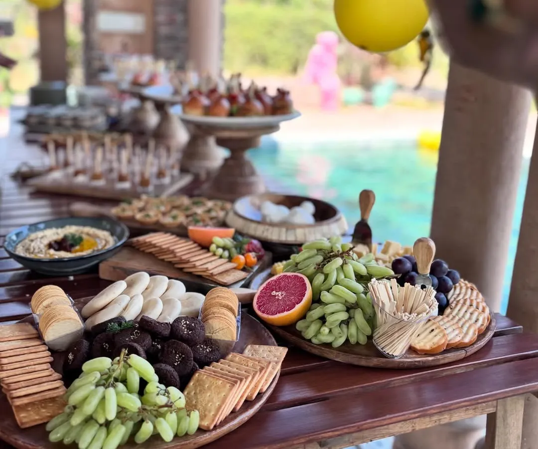 An abundant grazing table set for a sun-drenched poolside party. I customize each spread to match the event's theme, featuring a vibrant mix of fresh fruits, artisanal cheeses, crackers, and gourmet bites.