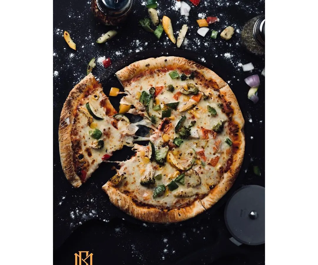 A dynamic overhead shot of a pizza, styled with scattered ingredients for an editorial feel. This dark, moody photography is perfect for restaurants wanting to create a premium, artisanal brand image.