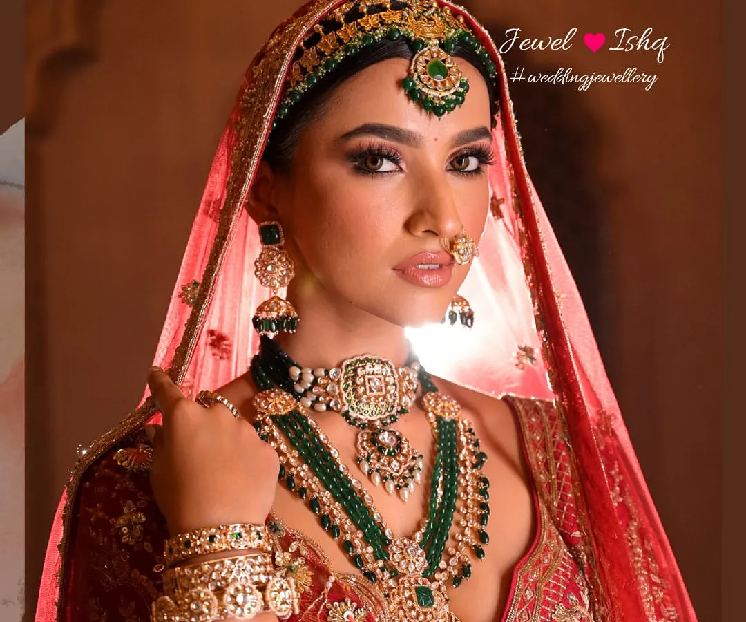 This is the ultimate royal bridal look. A heavily layered Kundan and Polki set with deep green emeralds, complete with a traditional mathapatti, jhumkas, and nath. Every piece is designed to make you feel like a queen on your wedding day.