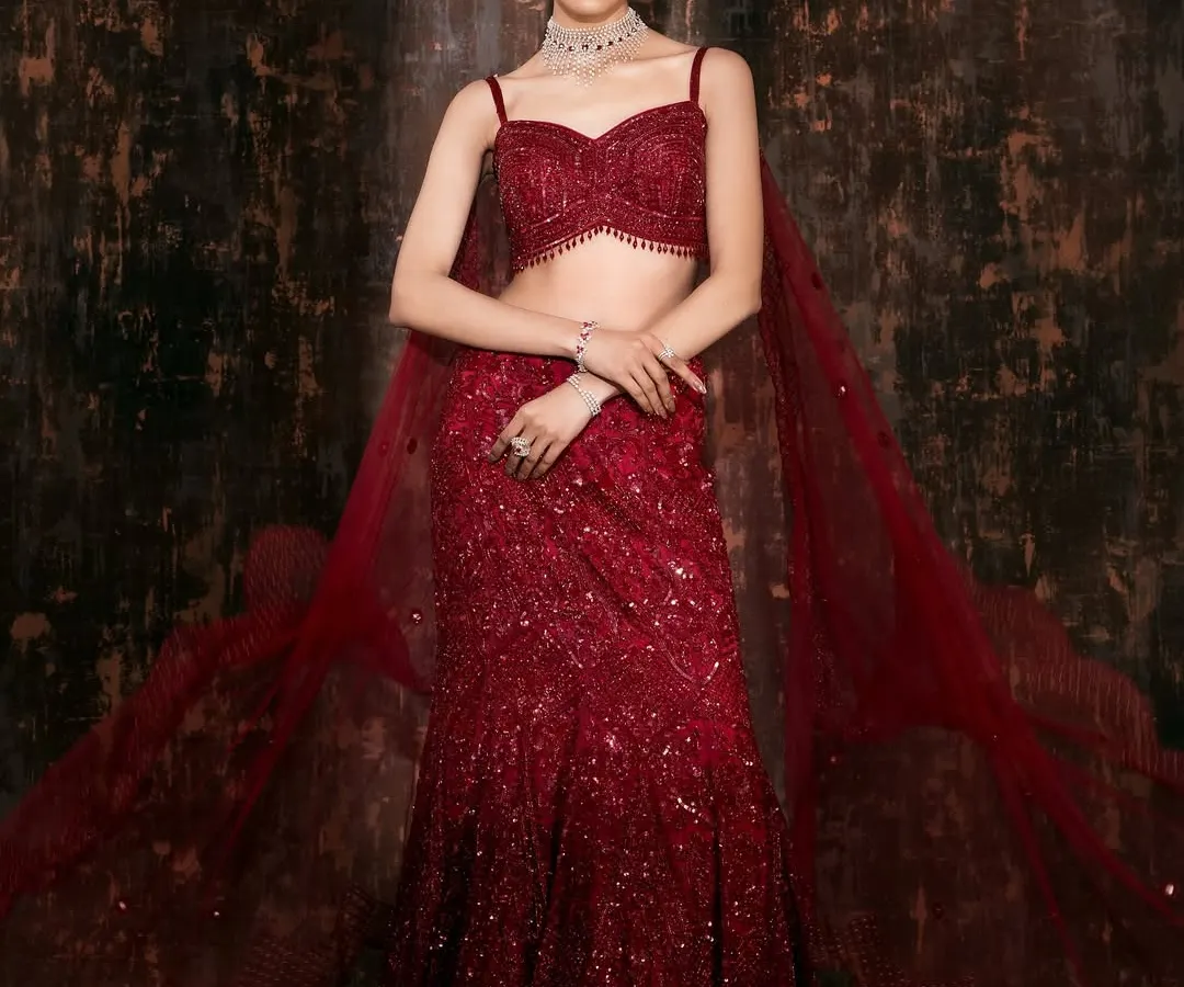 The full vision of a modern bridal look. The movement in the flowing red lehenga and the confident pose create a powerful silhouette against a moody, textured backdrop. This is how we build a complete story for a designer's collection.