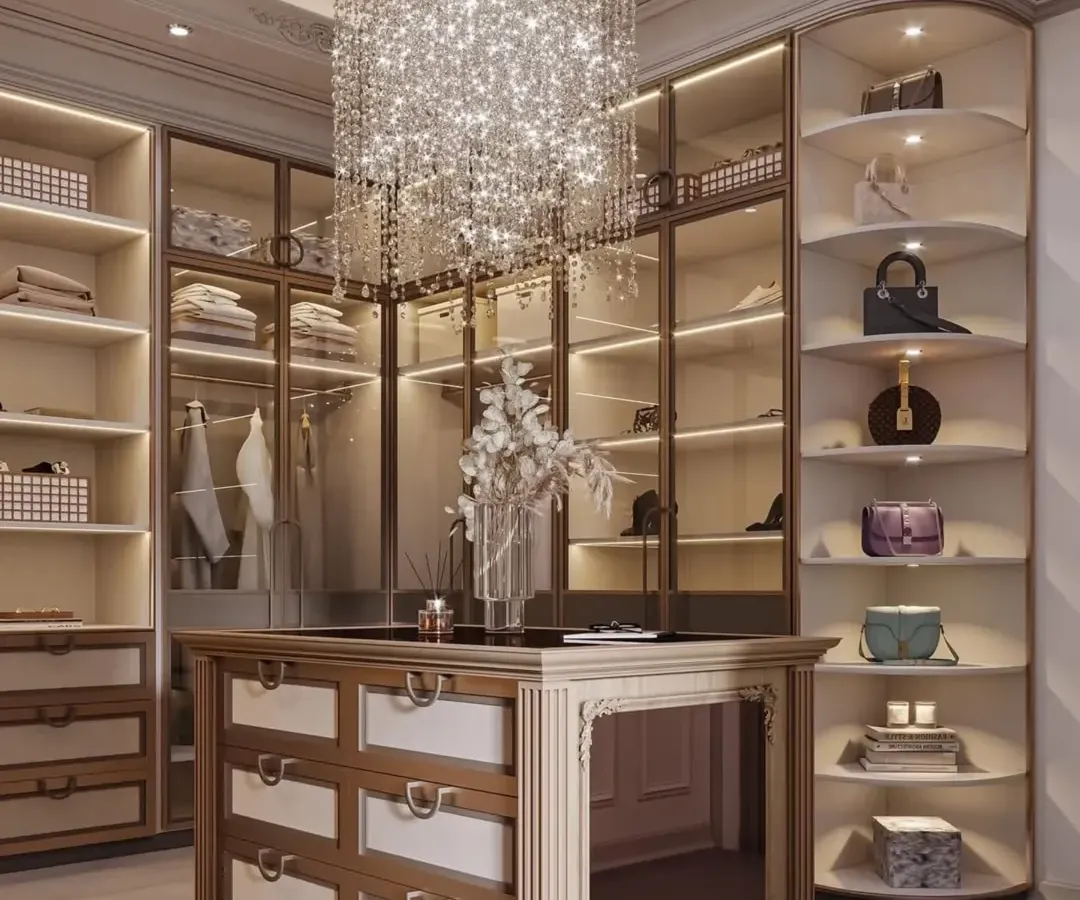 I design walk-in closets that are both a sanctuary and a statement. This space features a stunning crystal chandelier, custom glass-front cabinetry with internal lighting to display accessories, and a central island with organized drawer storage for a truly luxurious dressing experience.