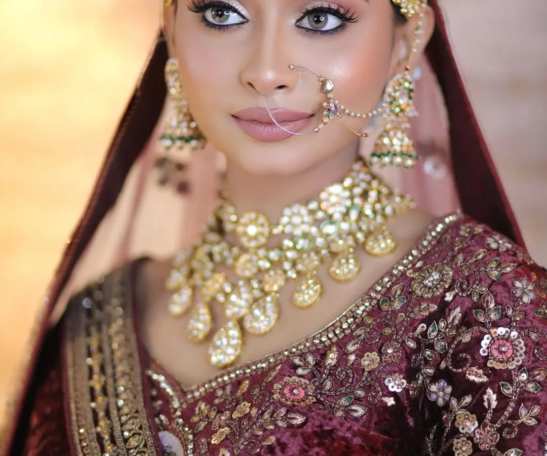 This is the epitome of royal elegance. A close-up of a stunning bridal look featuring a deep velvet maroon lehenga, flawless skin, and eyes that tell a story.