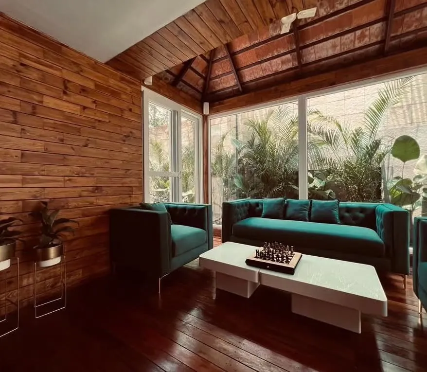 An elegant sunroom designed as a seamless extension of the home, featuring rich IPE wood flooring and paneling with a traditional Mangalore tile roof. The floor-to-ceiling glass walls invite the surrounding garden indoors, creating a tranquil retreat for any weather.
