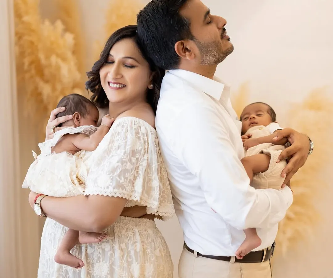 Welcoming newborn twins is double the blessing. In this serene studio portrait, a new mother and father stand back to back, each cradling one of their tiny miracles, capturing a moment of quiet joy and connection.