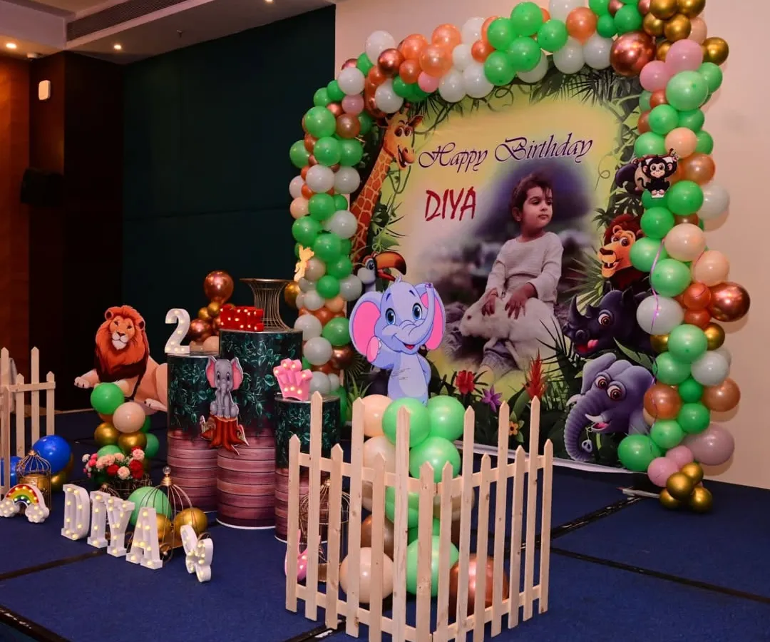 I bring the jungle to your party with this safari-themed setup. It features a personalized backdrop with the birthday child's photo, a green and orange balloon arch, and fun cutouts of jungle animals like lions and elephants.