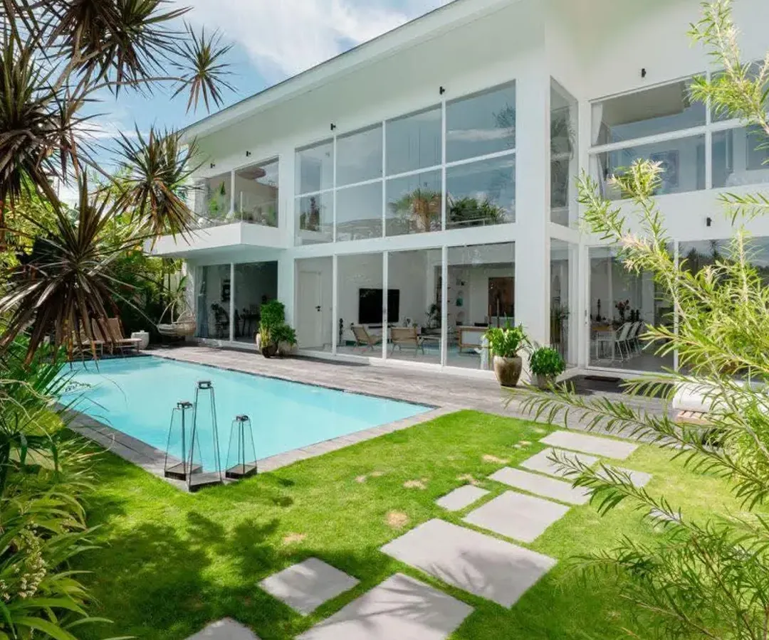 This modern villa features floor-to-ceiling windows that look out onto a tropical paradise. I used a combination of lush lawns, stone pavers, and mature palm trees to create a luxurious, resort-like feel right at home.