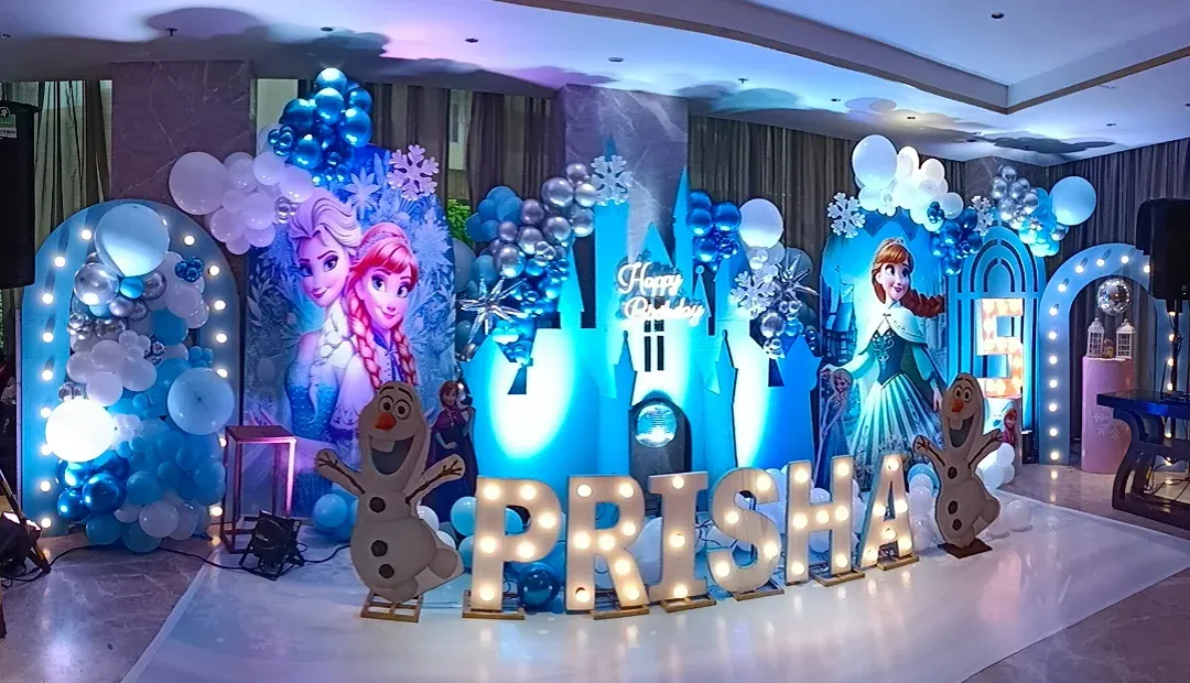Bringing the magic of Arendelle to life with a complete Frozen theme party setup. This includes character cutouts of Elsa, Anna, and Olaf, an illuminated ice castle backdrop, snowflake details, and a balloon garland in signature icy blue, white, and silver tones. The light-up marquee letters for the name make it extra special.