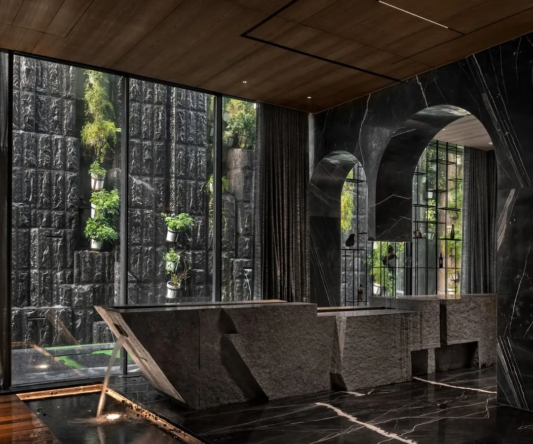 For the Green Court Villa, I designed this split stone bar counter to be the heart of the entertainment space. It's not just a functional element but a sculptural masterpiece that interacts with a tranquil water body, seamlessly merging the indoors with the calming presence of nature. This is how I create immersive guest experiences.