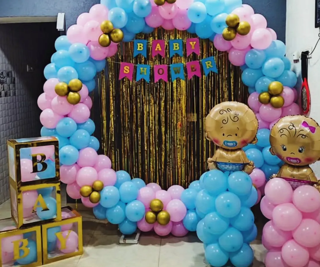 Celebrating with a splash of color. This baby shower setup is perfect for a gender reveal, with a full balloon ring in pink and blue, a sparkling gold backdrop, and cute baby-themed props to make the moment pop. 🎈
