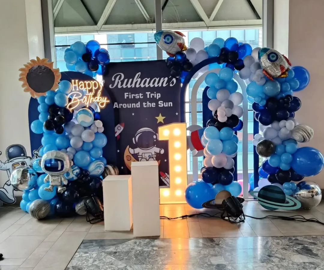 This is a complete "First Trip Around the Sun" space-themed setup for a first birthday party. I designed the entire scene with a custom backdrop, a full balloon arch in shades of blue, astronaut props, and a light-up marquee number '1'.