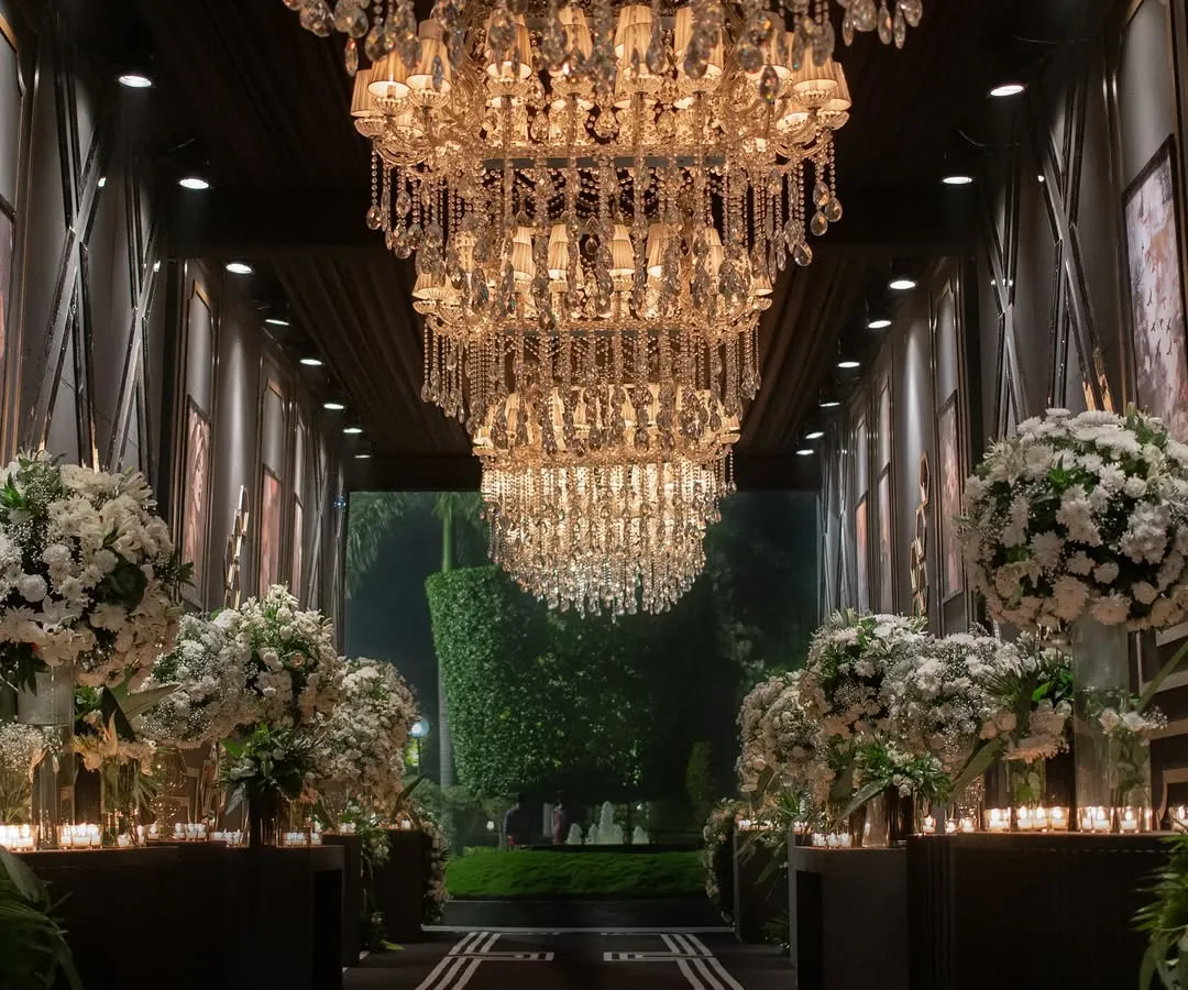 For a glamorous 25th-anniversary celebration, I designed this dramatic entryway. A grand hallway lined with massive crystal chandeliers and lush white floral arrangements set a sophisticated, high-energy tone for a night of black-tie opulence and dancing.