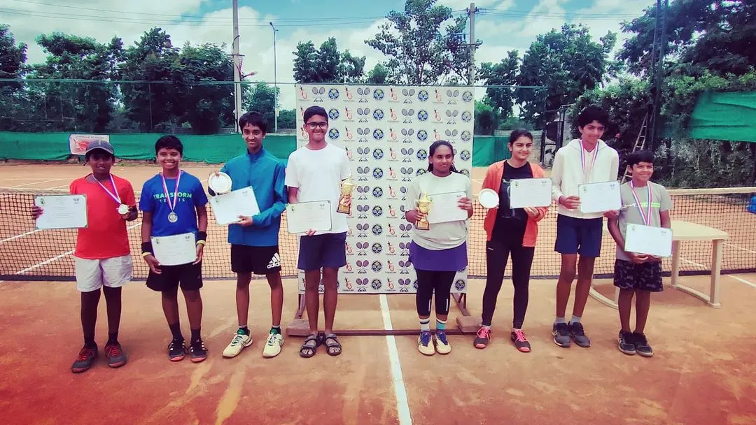 A group photo of all the winners and runners-up from the AITA TS7 Under-14 tournament, celebrating their achievements with trophies, medals, and certificates.