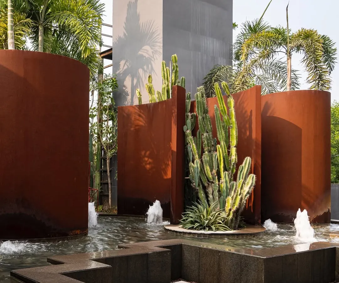 A sculptural water feature at the KEUS commercial hub. The design contrasts the industrial feel of rust-hued Corten steel walls with the organic forms of cacti and the movement of water, creating a bold, avant-garde landscape.